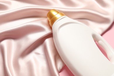 Photo of Bottle of fabric softener and beige cloth on pink background, above view