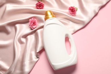 Photo of Bottle of fabric softener, flowers and beige cloth on pink background, flat lay