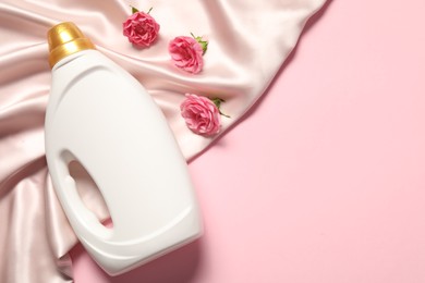 Photo of Bottle of fabric softener, flowers and beige cloth on pink background, flat lay. Space for text