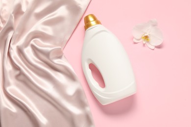 Photo of Bottle of fabric softener, orchid flower and beige cloth on pink background, flat lay