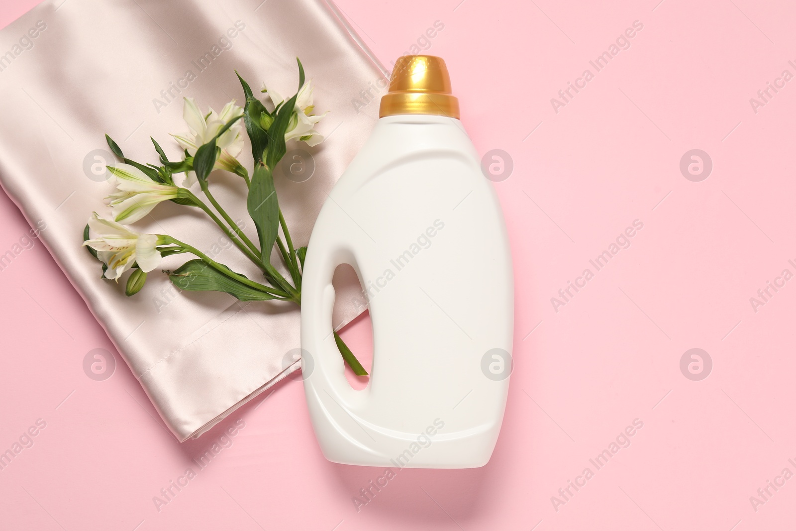 Bottle of fabric softener, flowers and beige cloth on pink background, flat lay Photo of Bottle of fabric softener, flowers and beige cloth on pink background, flat lay