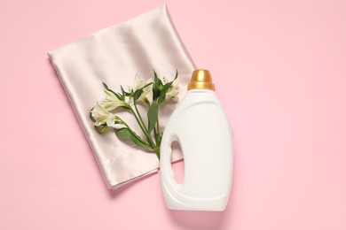 Photo of Bottle of fabric softener, flowers and beige cloth on pink background, flat lay