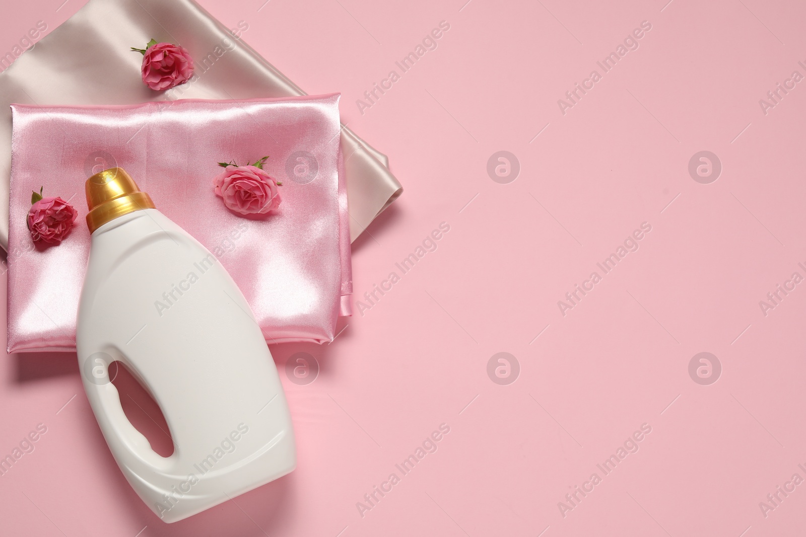 Bottle of fabric softener, flowers and color fabrics on pink background, flat lay. Space for text Photo of Bottle of fabric softener, flowers and color fabrics on pink background, flat lay. Space for text