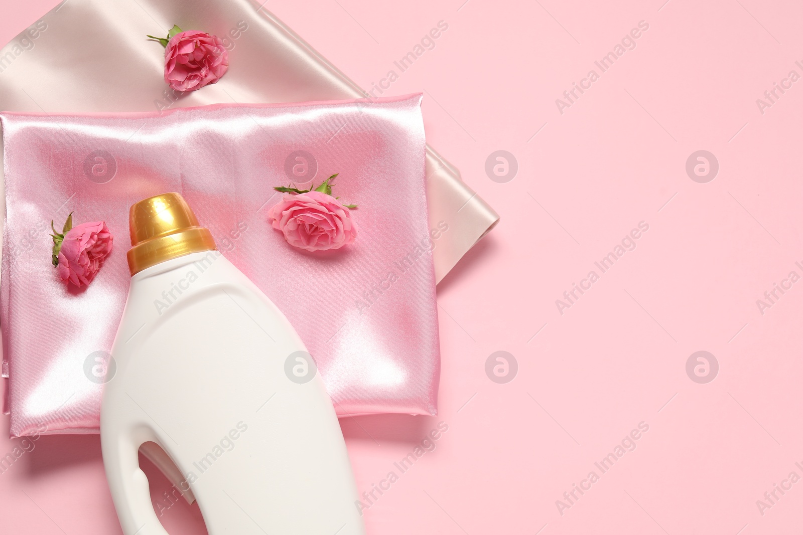 Bottle of fabric softener, flowers and color fabrics on pink background, flat lay. Space for text Photo of Bottle of fabric softener, flowers and color fabrics on pink background, flat lay. Space for text