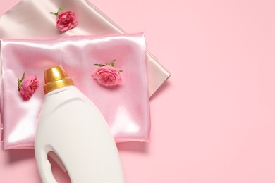 Photo of Bottle of fabric softener, flowers and color fabrics on pink background, flat lay. Space for text