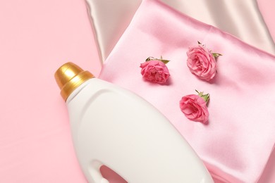 Photo of Bottle of fabric softener, flowers and color fabrics on pink background, flat lay