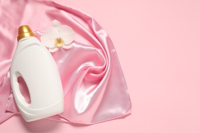 Photo of Bottle of fabric softener, orchid flower and color cloth on pink background, flat lay. Space for text