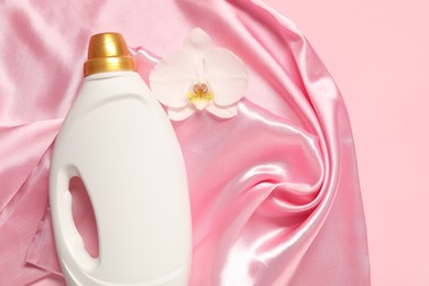 Photo of Bottle of fabric softener, orchid flower and color cloth on pink background, flat lay