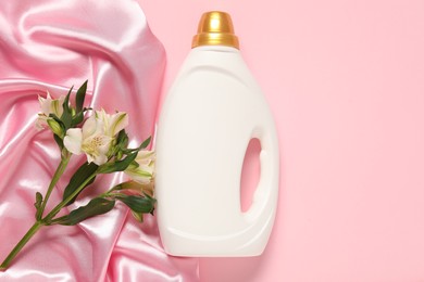 Photo of Bottle of fabric softener, flowers and color cloth on pink background, flat lay