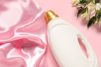Photo of Bottle of fabric softener, flowers and color cloth on pink background, flat lay