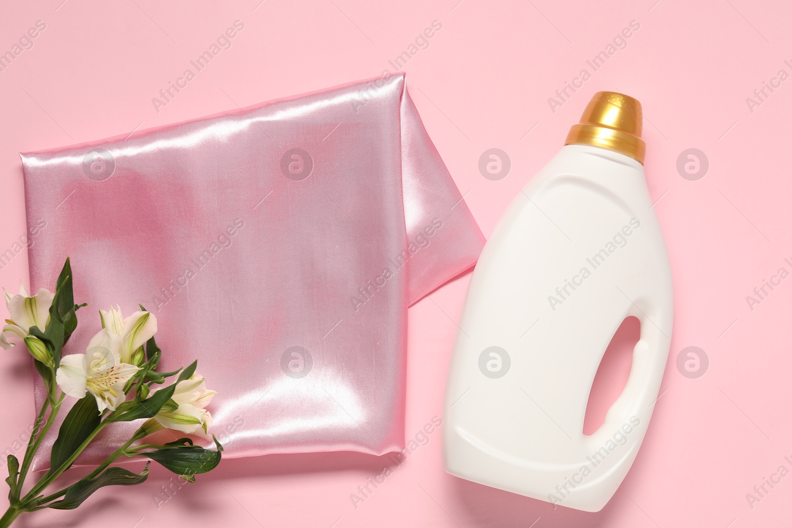Bottle of fabric softener, flowers and color cloth on pink background, flat lay Photo of Bottle of fabric softener, flowers and color cloth on pink background, flat lay
