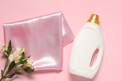 Photo of Bottle of fabric softener, flowers and color cloth on pink background, flat lay