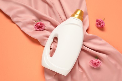 Photo of Bottle of fabric softener, flowers and pink cloth on coral background, flat lay