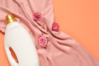 Photo of Bottle of fabric softener, flowers and pink cloth on coral background, flat lay