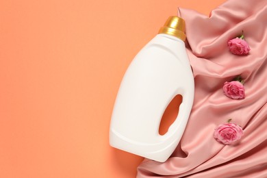 Photo of Bottle of fabric softener, flowers and pink cloth on coral background, flat lay. Space for text