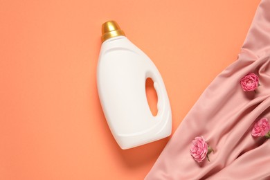 Photo of Bottle of fabric softener, flowers and pink cloth on coral background, flat lay