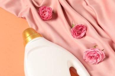 Photo of Bottle of fabric softener, flowers and pink cloth on coral background, above view