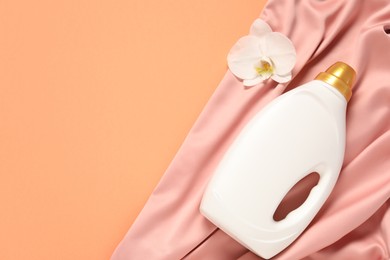 Photo of Bottle of fabric softener, orchid flower and pink cloth on coral background, flat lay. Space for text
