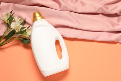 Photo of Bottle of fabric softener, flowers and pink cloth on coral background, flat lay