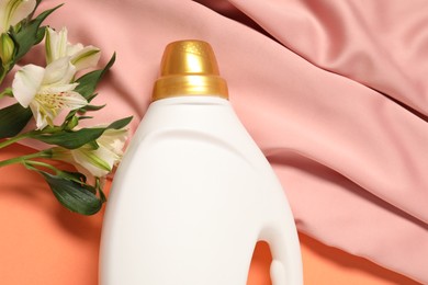 Photo of Bottle of fabric softener, flowers and pink cloth on coral background, flat lay