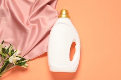 Photo of Bottle of fabric softener, flowers and pink cloth on coral background, flat lay