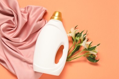 Photo of Bottle of fabric softener, flowers and pink cloth on coral background, flat lay