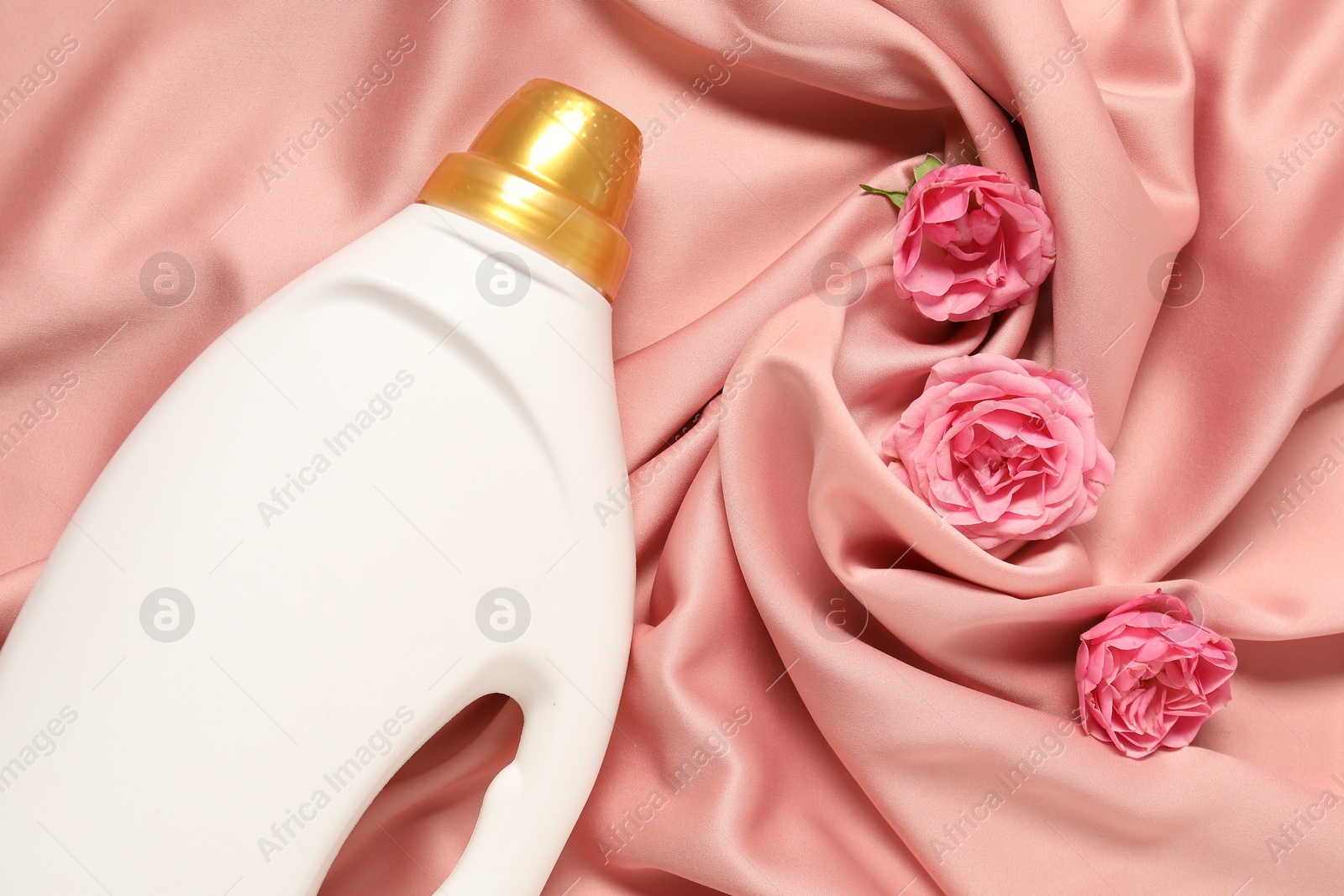 Bottle of fabric softener and flowers on pink cloth, flat lay Photo of Bottle of fabric softener and flowers on pink cloth, flat lay