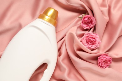 Photo of Bottle of fabric softener and flowers on pink cloth, flat lay