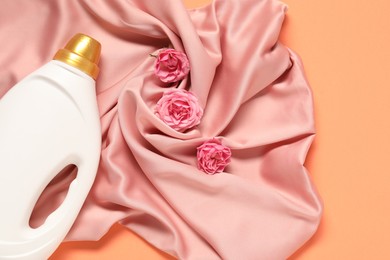 Photo of Bottle of fabric softener, flowers and pink cloth on coral background, flat lay