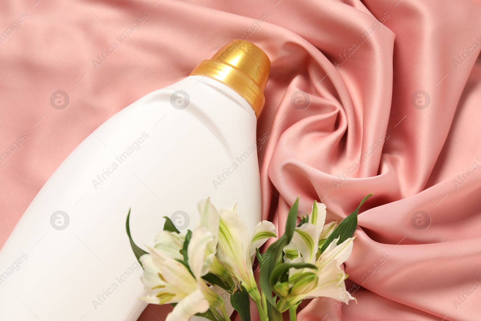 Bottle of fabric softener and flowers on pink cloth, above view Photo of Bottle of fabric softener and flowers on pink cloth, above view