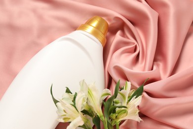 Photo of Bottle of fabric softener and flowers on pink cloth, above view