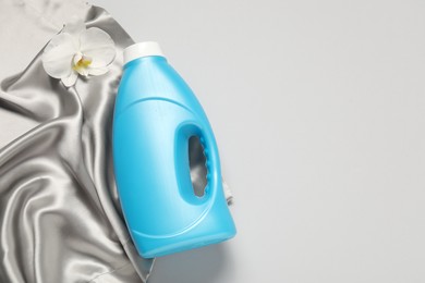 Photo of Bottle of fabric softener, orchid flower and color cloth on light grey background, flat lay. Space for text