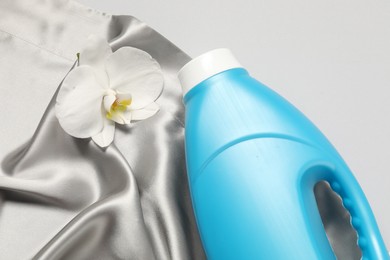 Photo of Bottle of fabric softener, orchid flower and color cloth on light grey background, above view