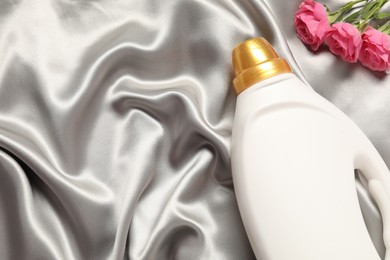 Photo of Bottle of fabric softener and flowers on grey cloth, flat lay. Space for text
