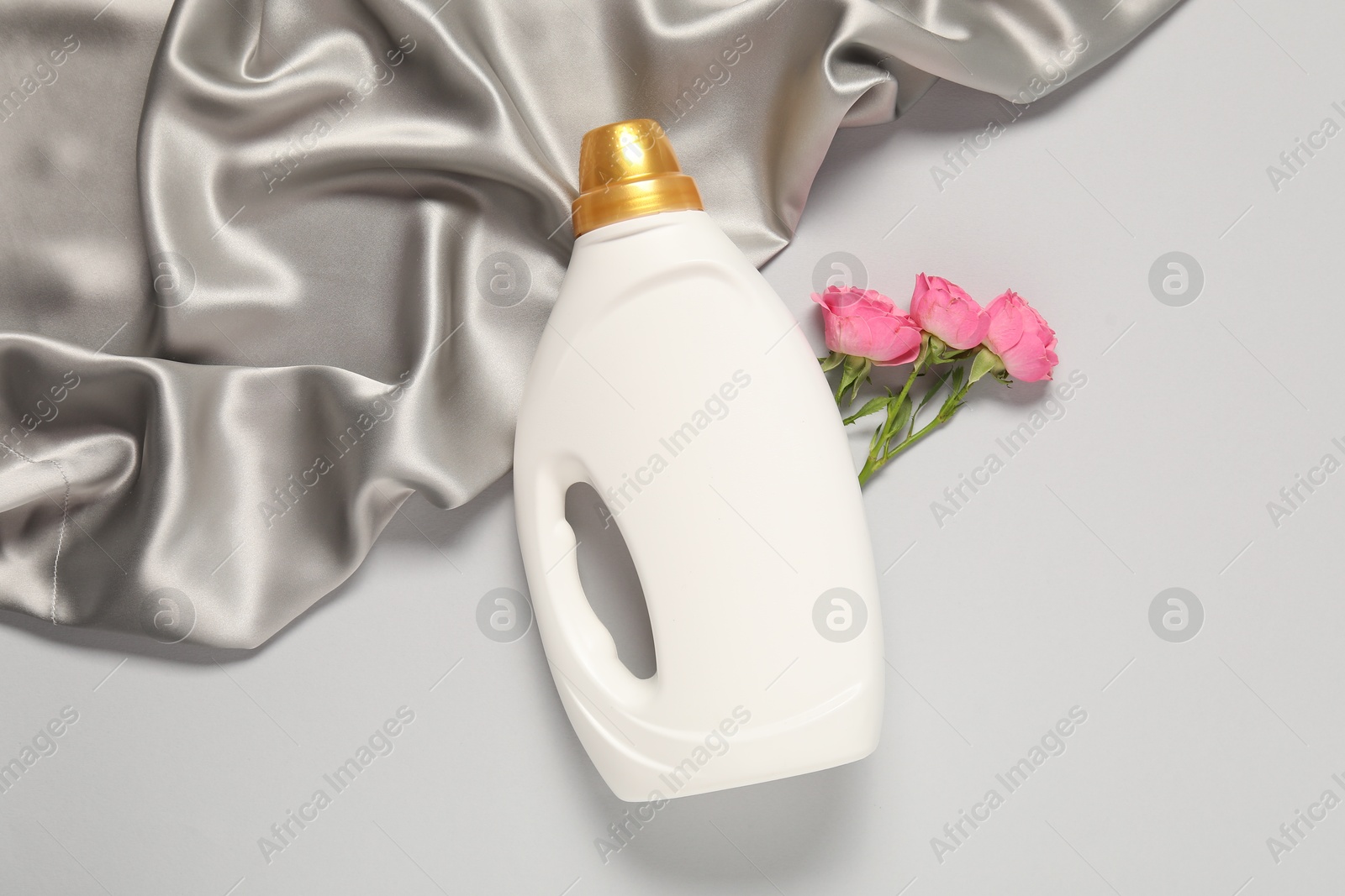Bottle of fabric softener, flowers and color cloth on light grey background, flat lay Photo of Bottle of fabric softener, flowers and color cloth on light grey background, flat lay
