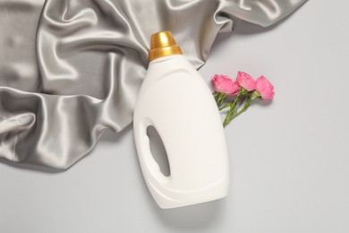 Photo of Bottle of fabric softener, flowers and color cloth on light grey background, flat lay