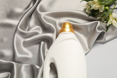 Photo of Bottle of fabric softener, flowers and color cloth on light grey background, above view