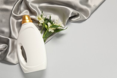 Photo of Bottle of fabric softener, flowers and color cloth on light grey background, flat lay. Space for text