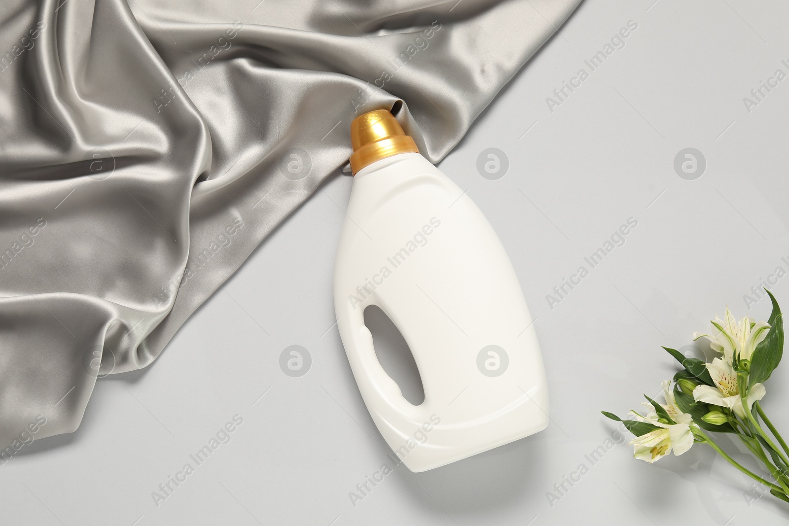 Bottle of fabric softener, flowers and color cloth on light grey background, flat lay Photo of Bottle of fabric softener, flowers and color cloth on light grey background, flat lay