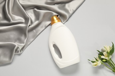 Photo of Bottle of fabric softener, flowers and color cloth on light grey background, flat lay