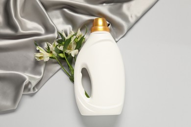 Photo of Bottle of fabric softener, flowers and color cloth on light grey background, flat lay