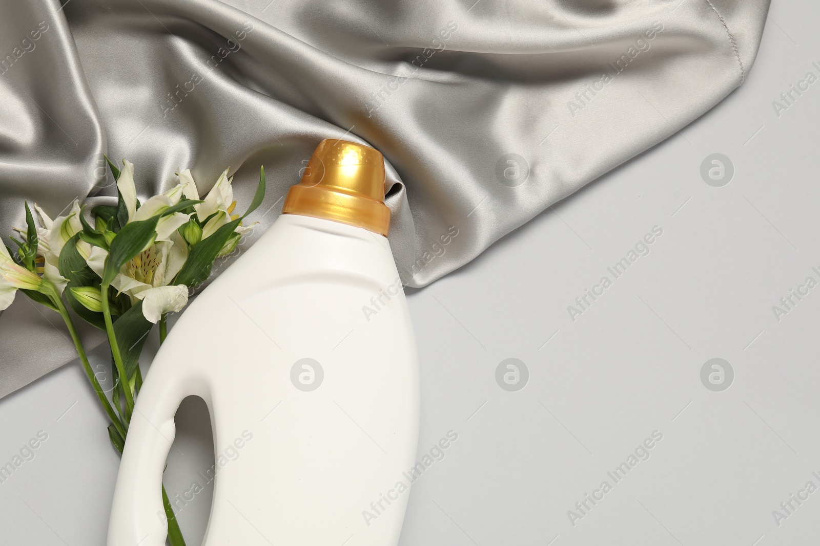 Bottle of fabric softener, flowers and color cloth on light grey background, flat lay. Space for text Photo of Bottle of fabric softener, flowers and color cloth on light grey background, flat lay. Space for text