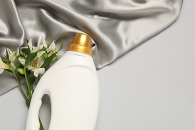 Photo of Bottle of fabric softener, flowers and color cloth on light grey background, flat lay. Space for text