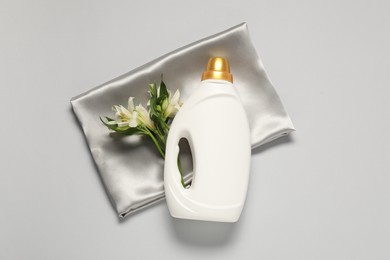 Photo of Bottle of fabric softener, flowers and color cloth on light grey background, flat lay
