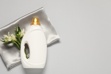 Photo of Bottle of fabric softener, flowers and color cloth on light grey background, flat lay. Space for text