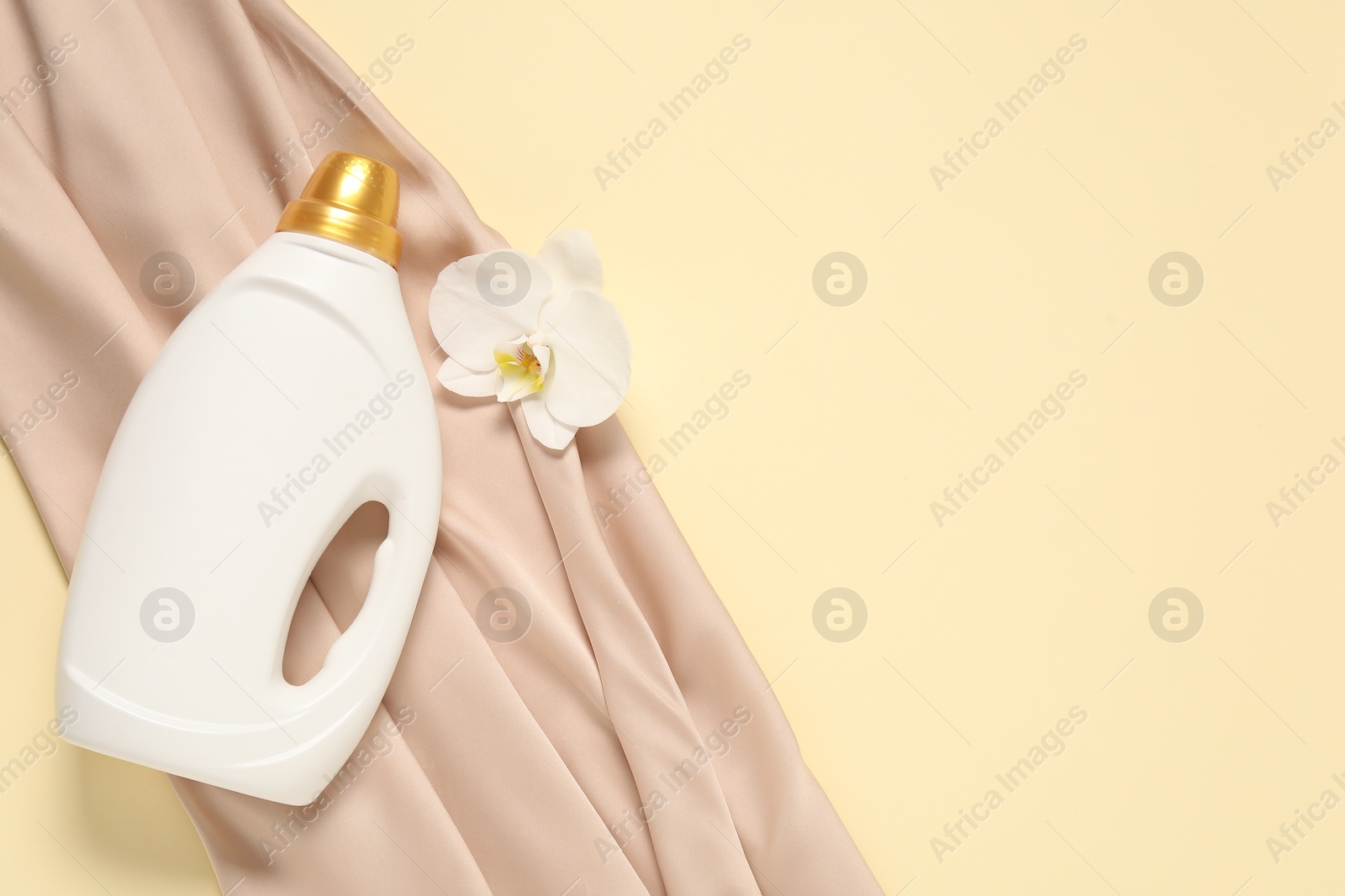 Bottle of fabric softener, orchid flower and color cloth on beige background, flat lay. Space for text Photo of Bottle of fabric softener, orchid flower and color cloth on beige background, flat lay. Space for text