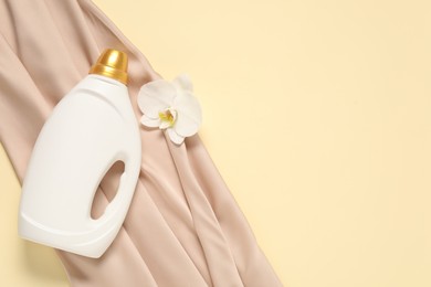 Photo of Bottle of fabric softener, orchid flower and color cloth on beige background, flat lay. Space for text