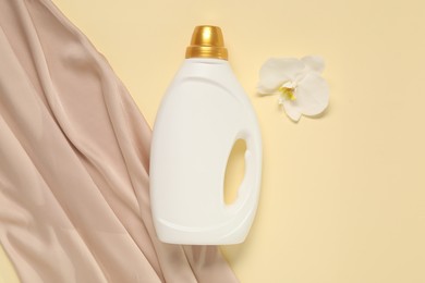 Photo of Bottle of fabric softener, orchid flower and color cloth on beige background, flat lay