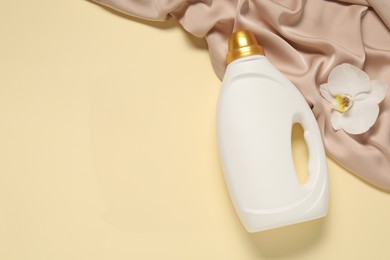Photo of Bottle of fabric softener, orchid flower and color cloth on beige background, flat lay. Space for text