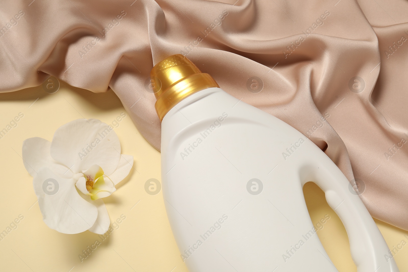 Bottle of fabric softener, orchid flower and color cloth on beige background, flat lay Photo of Bottle of fabric softener, orchid flower and color cloth on beige background, flat lay